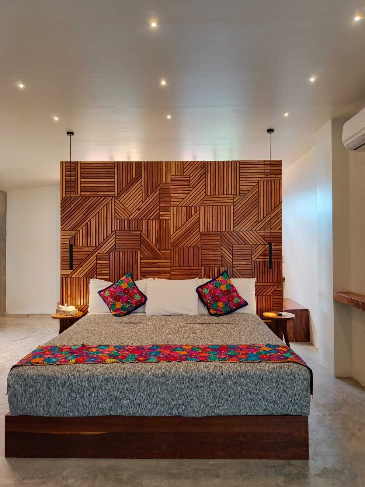 Un dormitorio moderno con una cabecera de madera con diseño geométrico, una cama grande con colcha estampada y dos mesitas de noche con lámparas.