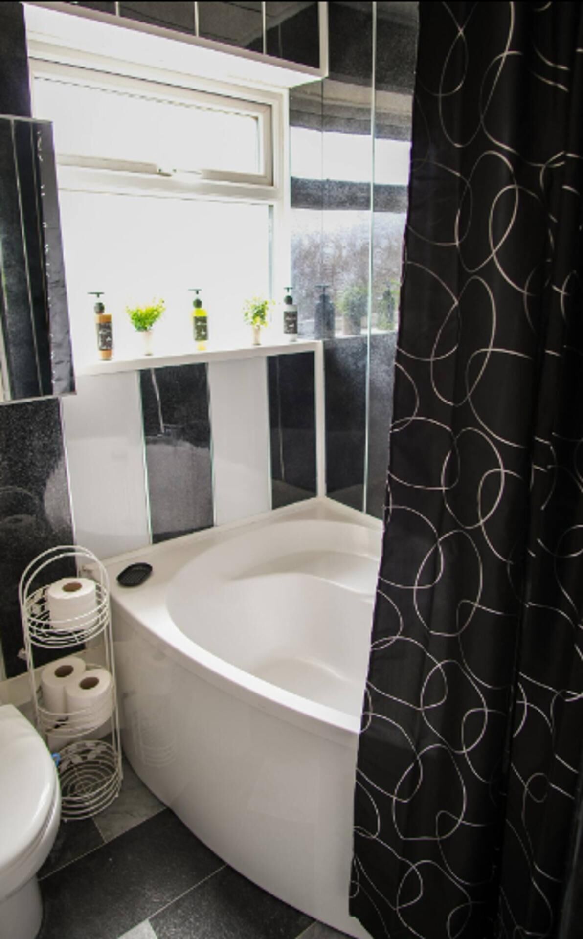 A bathroom with a bathtub, toilet, and a shelf with toiletries.