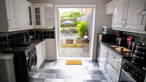 A compact kitchen with white cabinets, a black countertop, and a built-in washing machine. - South Shield Seaside Retreat (South Shields)