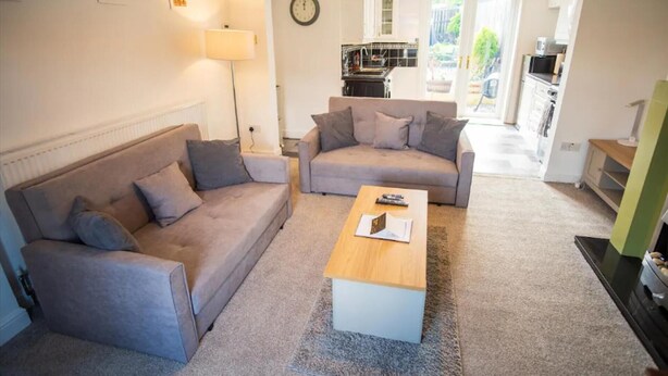 A living room with two sofas, a coffee table, and a lamp. There is a kitchen visible through an open door. - South Shield Seaside Retreat (South Shields)