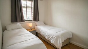 A small, clean room with two single beds, a bedside table with a lamp, and a window with curtains. - South Shield Seaside Retreat (South Shields)