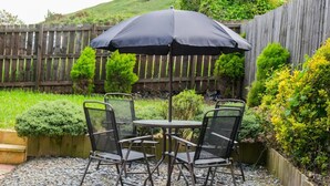 A patio area with a table and four chairs, an umbrella, and a wooden fence in the background. - South Shield Seaside Retreat (South Shields)