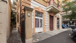 Une rue étroite bordée d’immeubles, avec un magasin fermé et des voitures garées.
