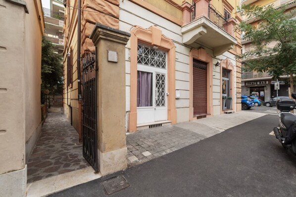 A narrow street with buildings, a closed shop, and parked cars.