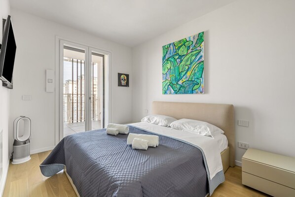 A hotel room with a bed, a bedside table, a wall-mounted TV, and a large window.