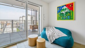 Un salón moderno con un sofá color turquesa, una obra de arte colorida y vistas de la ciudad a través de un amplio ventanal corredera.