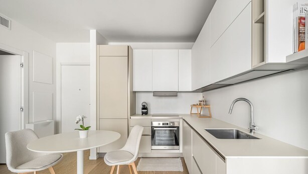 Una cocina moderna con armarios blancos, horno empotrado, lavamanos y un comedor con mesa y sillas.