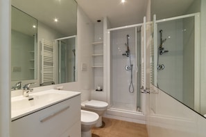 A modern bathroom with a glass-enclosed shower, a white sink, and a toilet.