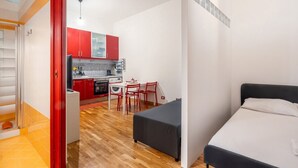 Una habitación compacta con cama, un pequeño kitchenette, una zona de comedor con sillas y una lavadora.
