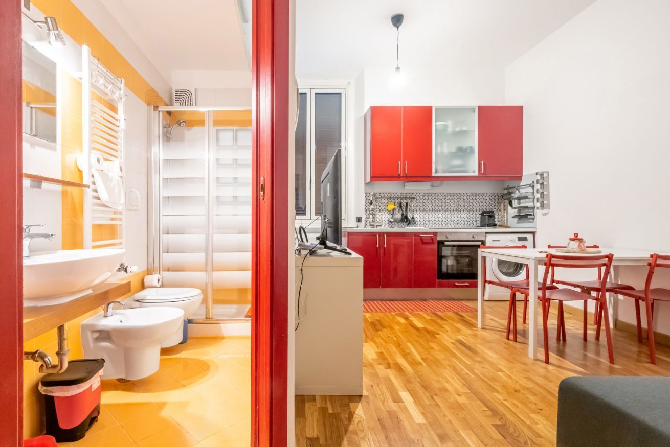 A compact kitchen with red cabinets, a white sink, and a dining area with red chairs.
