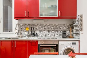 A kitchen with red cabinets, a sink, a stove, an oven, and a washing machine.