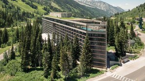 A modern hotel with a glass facade, surrounded by dense forest and mountains. - 2BR Cliff Club Retreat – Ski-In/Ski-Out! (Sandy)