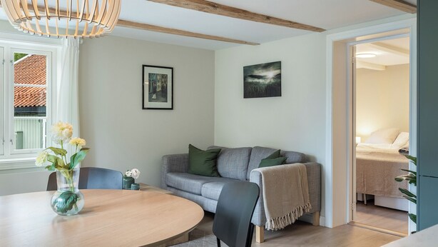 Un salon moderne avec une table ronde en bois, des chaises noires, un canapé gris et un luminaire suspendu.