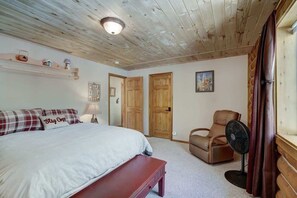 Een slaapkamer met een bed, een stoel, een ventilator en houten deuren.