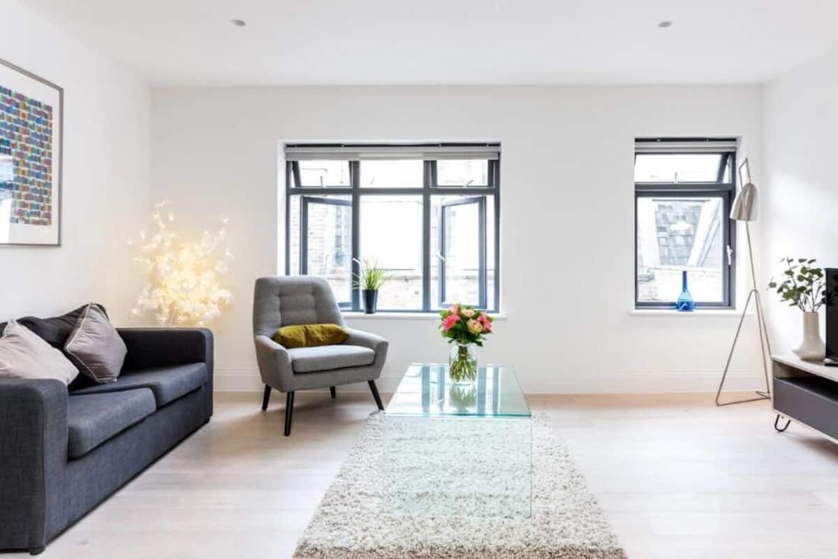 A modern living room with a sofa, armchair, glass coffee table, and a TV on a stand.