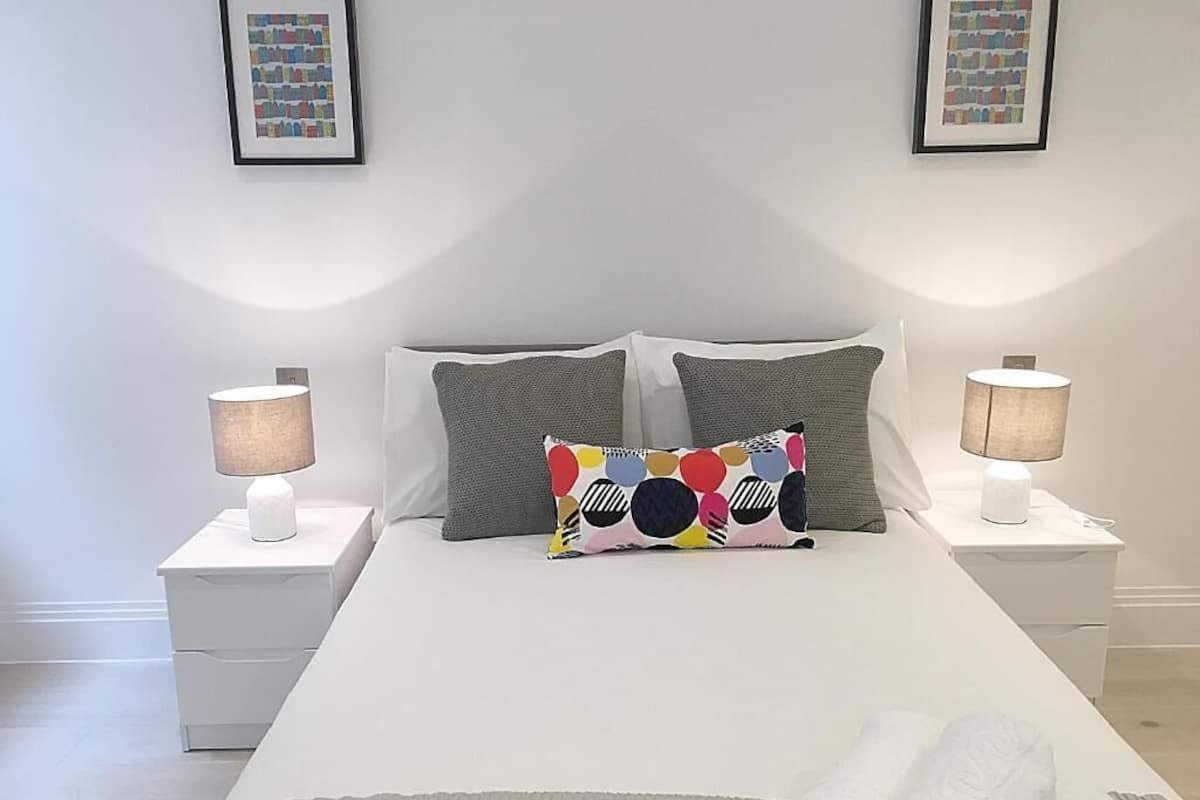 A neatly made bed with two pillows, a colorful pillow, and two bedside lamps on white nightstands.