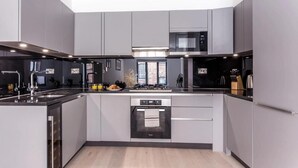 A modern kitchen with grey cabinetry, a black countertop, and a built-in dishwasher. - Oxford Circus Apartments (London)