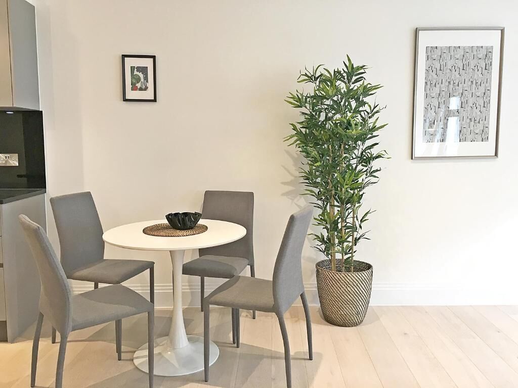 A dining area with a round table, four grey chairs, a potted plant, and two framed pictures on the wall.