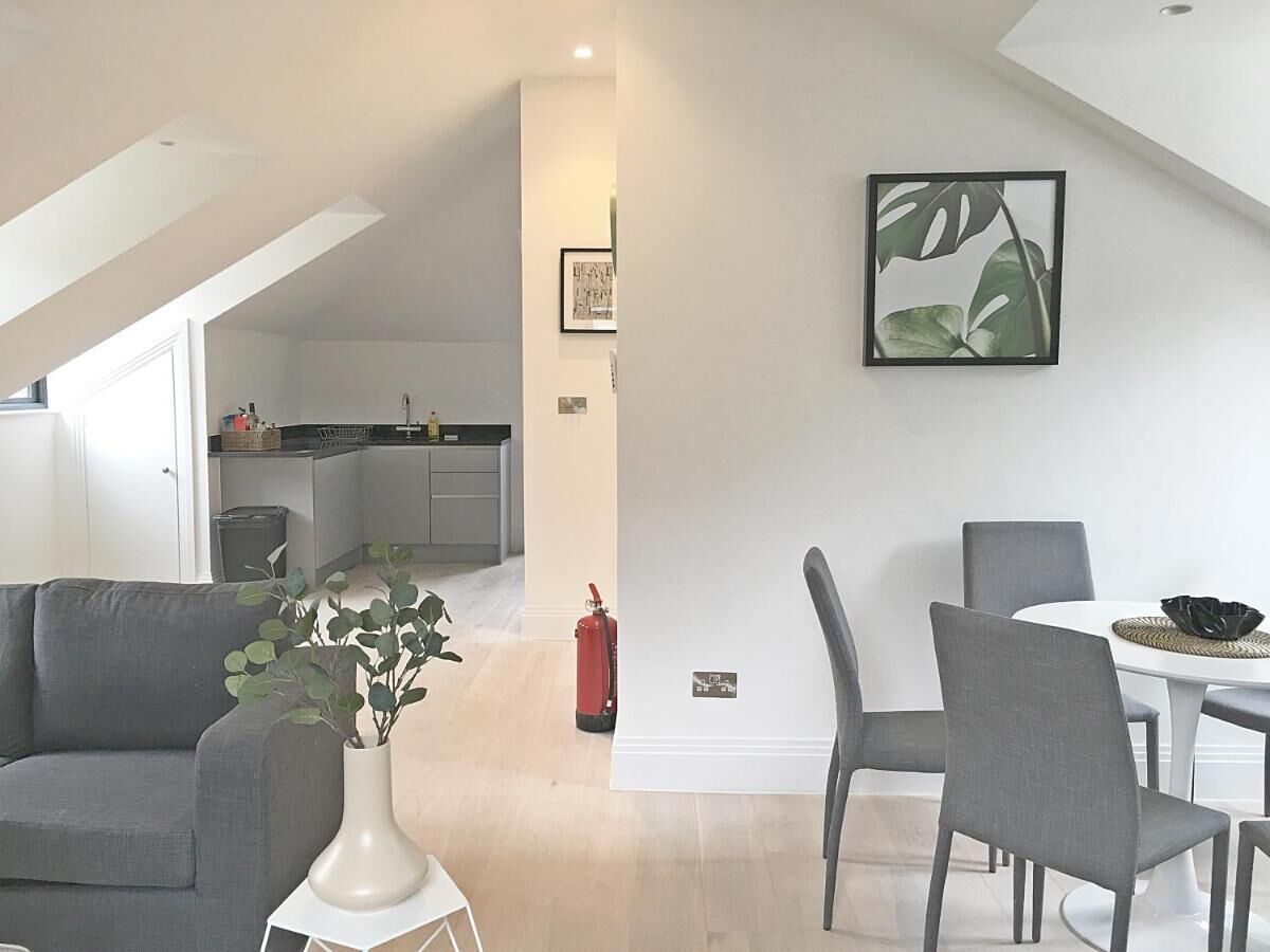 Una sala de estar moderna con un sofá, una mesa de comedor con sillas, un florero con plantas y una cocina al fondo.
