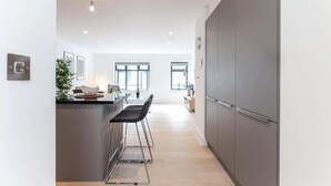 A modern kitchen with a central island, bar stools, and a large grey cabinet. - Oxford Circus Apartments (London)