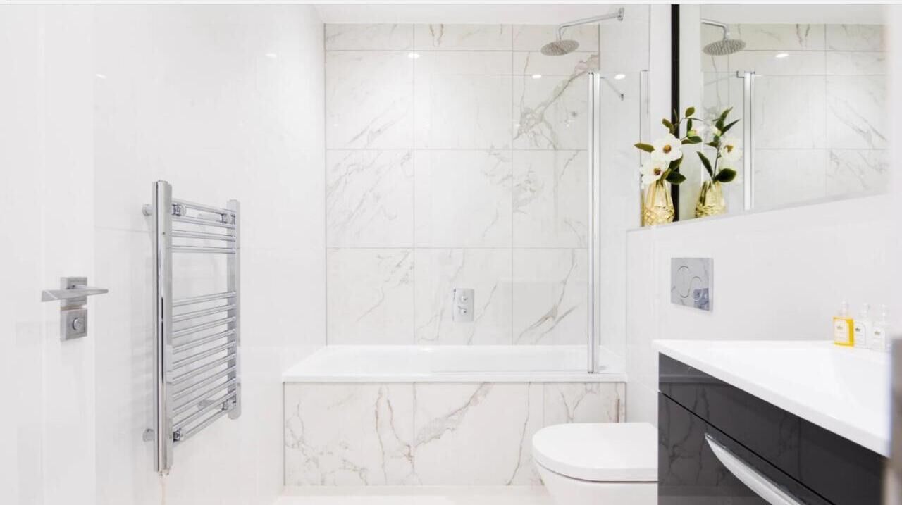 A modern bathroom with a glass-enclosed shower, a white toilet, and a marble-tiled wall.