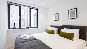 A modern hotel room with a large bed, two pillows, a window, and two framed pictures on the wall. - Oxford Circus Apartments (London)