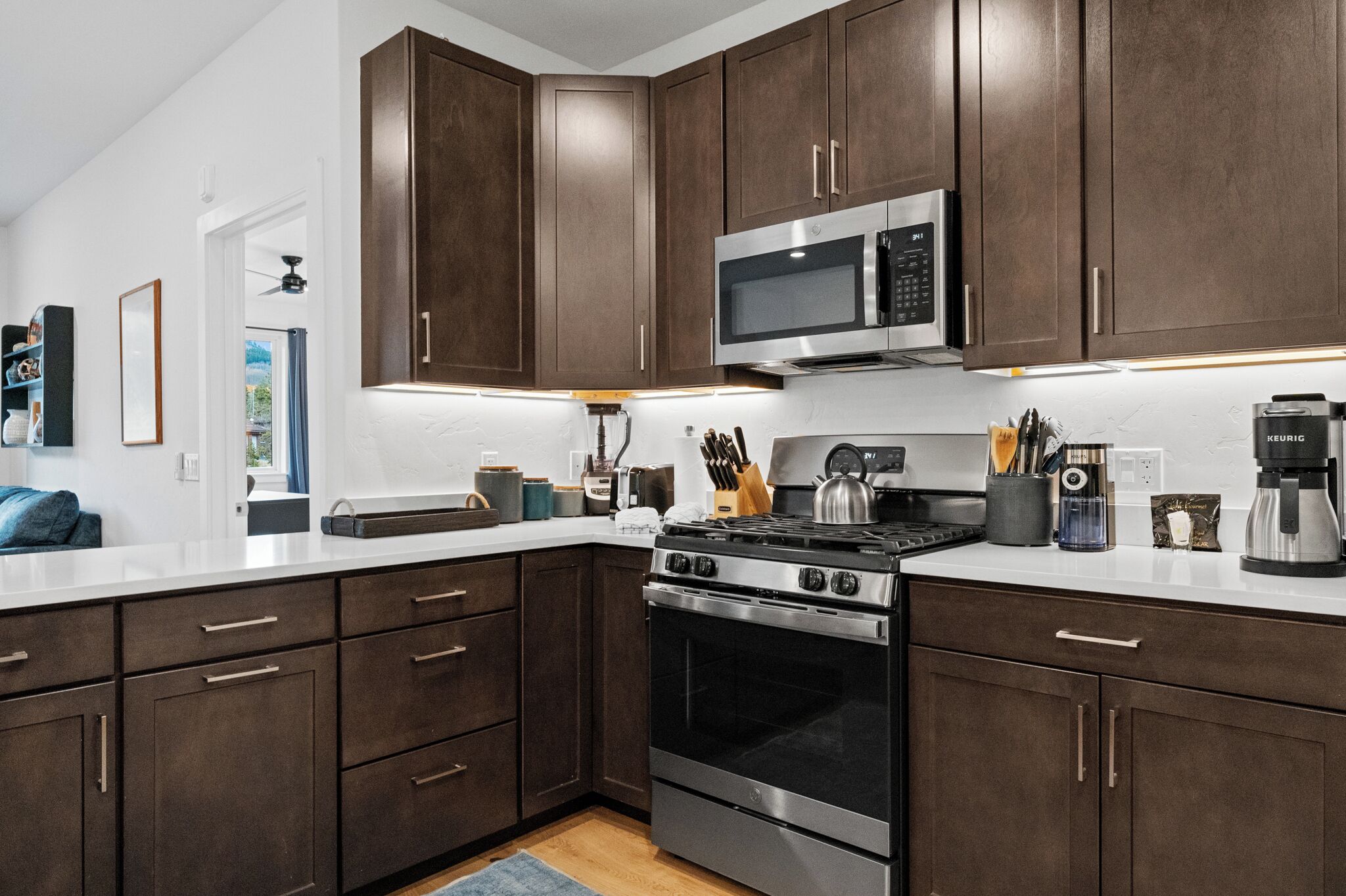 A modern kitchen with dark wood cabinets, stainless steel appliances, and a white countertop.