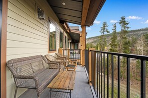 A covered porch with wicker furniture, a wooden table, and a view of a forested hillside. - Cl1302k-2 (Keystone)