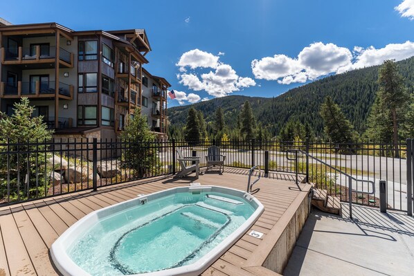 A wooden deck with a hot tub, a fenced area, and a mountain backdrop.