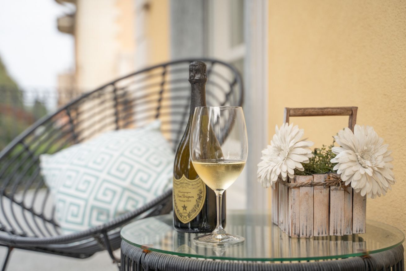 A bottle of wine, a glass, and a flower arrangement on a glass table.