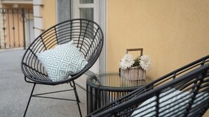 A wicker chair with a patterned cushion, a glass table with a flower vase, and a balcony railing. - Dimora Adriani on the Noble Floor, Charm & Relax in the Heart of Langhe (Cherasco)