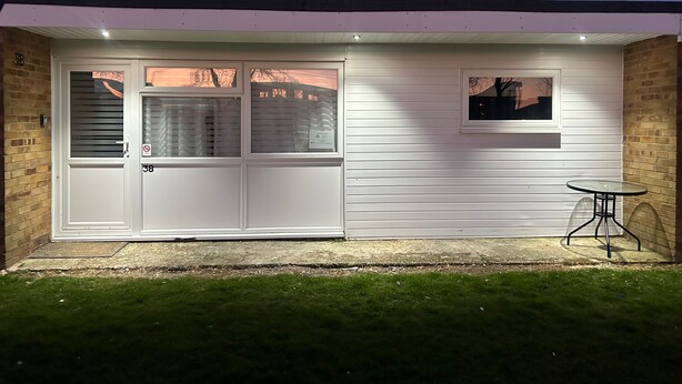 A house with a white exterior, a front door, and a small table with a chair outside. - Chalet for Hire in Florida Hemsby (Great Yarmouth)