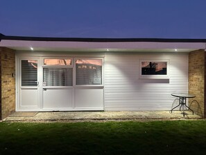A house with a white exterior, a front door, and a small table with a chair outside. - Chalet for Hire in Florida Hemsby (Great Yarmouth)