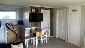 A compact kitchen with a dining area, a TV mounted above the counter, and a window providing natural light. - Chalet for Hire in Florida Hemsby (Great Yarmouth)