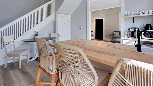 Une cuisine moderne avec une table à manger en bois et des chaises en osier, un escalier et une machine à café.