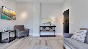 Un salon moderne avec un canapé gris, un fauteuil gris, une console noire agrémentée de paniers, un pouf rond et un téléviseur à écran plat fixé au mur.
