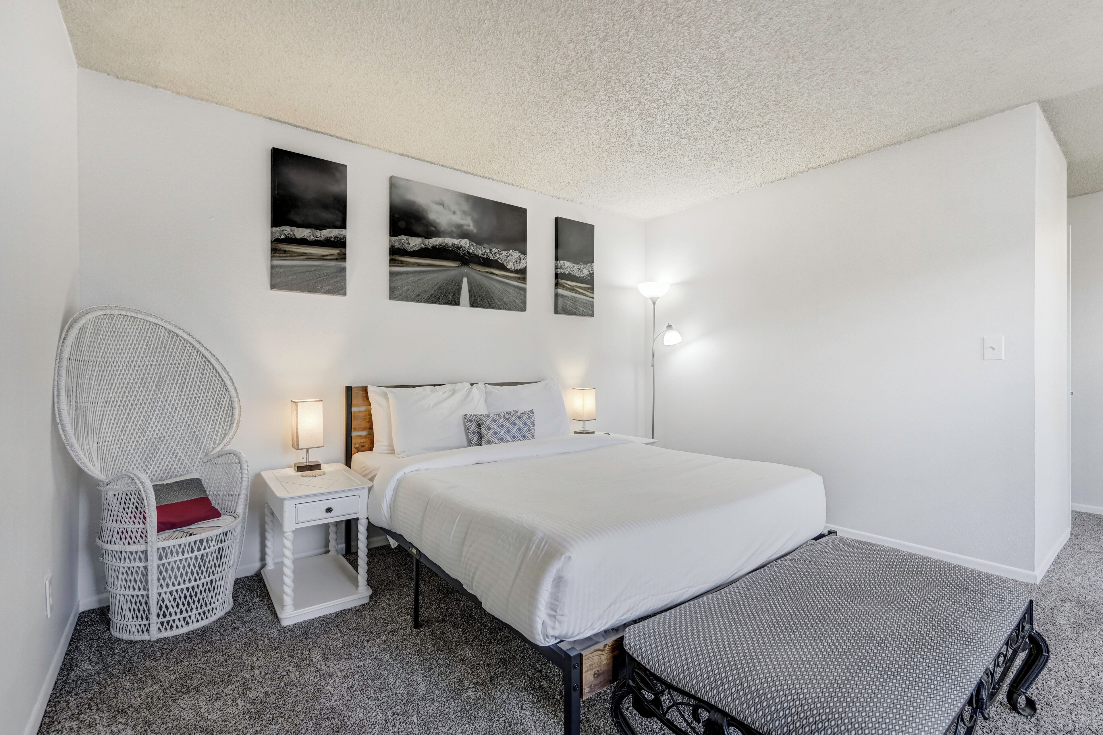 A bedroom with a bed, a nightstand, a chair, and wall art.