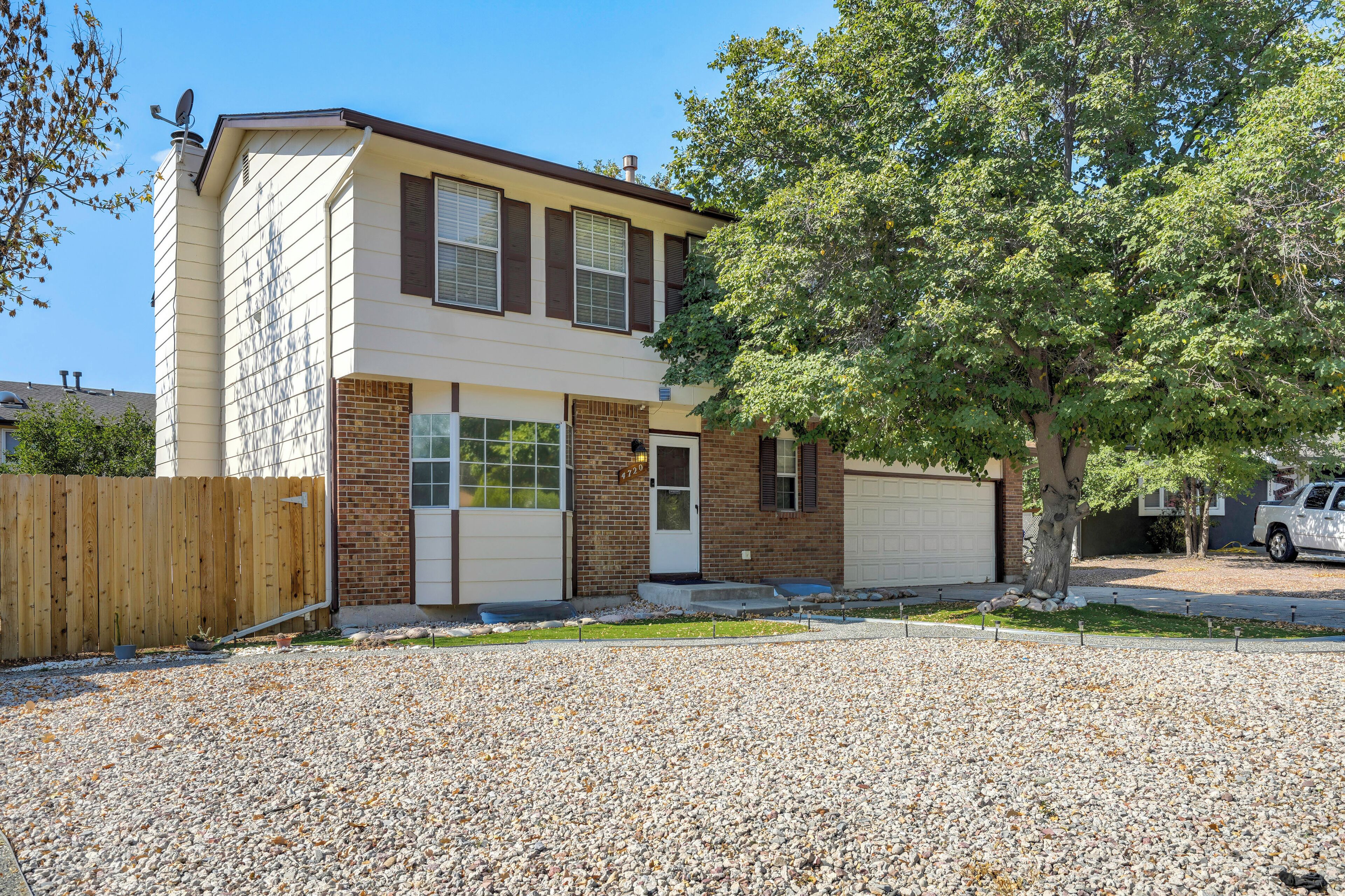 A two-story house with a garage, a gravel driveway, and a wooden fence.