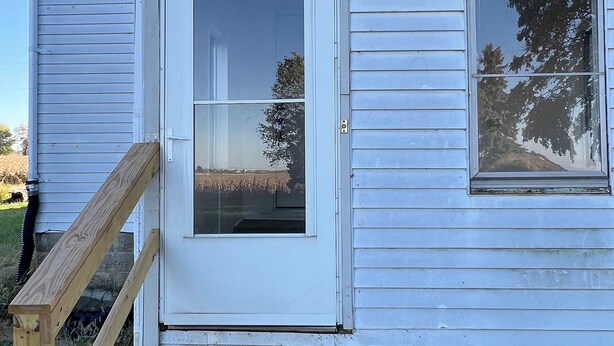 A white house with a front door, a small window, and a wooden handrail leading to the door.