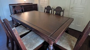 A dining room with a large wooden table, six chairs, a sideboard, and a door.