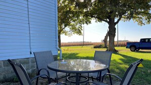 A patio with a round glass table and four chairs, a blue truck in the background, and a field of crops.