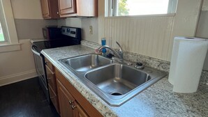 A kitchen with wooden cabinets, a granite countertop, stainless steel sink, and a window with a view.