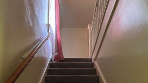A carpeted staircase with a wooden handrail and a red curtain at the top.