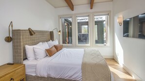 A bedroom with a bed, bedside tables, a window, and a wall-mounted TV. - Luxury 7 Bedroom Home + Hot Tub + Views of Lone Peak (Big Sky)