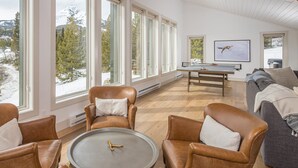 A spacious living room with leather chairs, a coffee table, and a sofa. Large windows offer a view of a snowy landscape. - Luxury 7 Bedroom Home + Hot Tub + Views of Lone Peak (Big Sky)