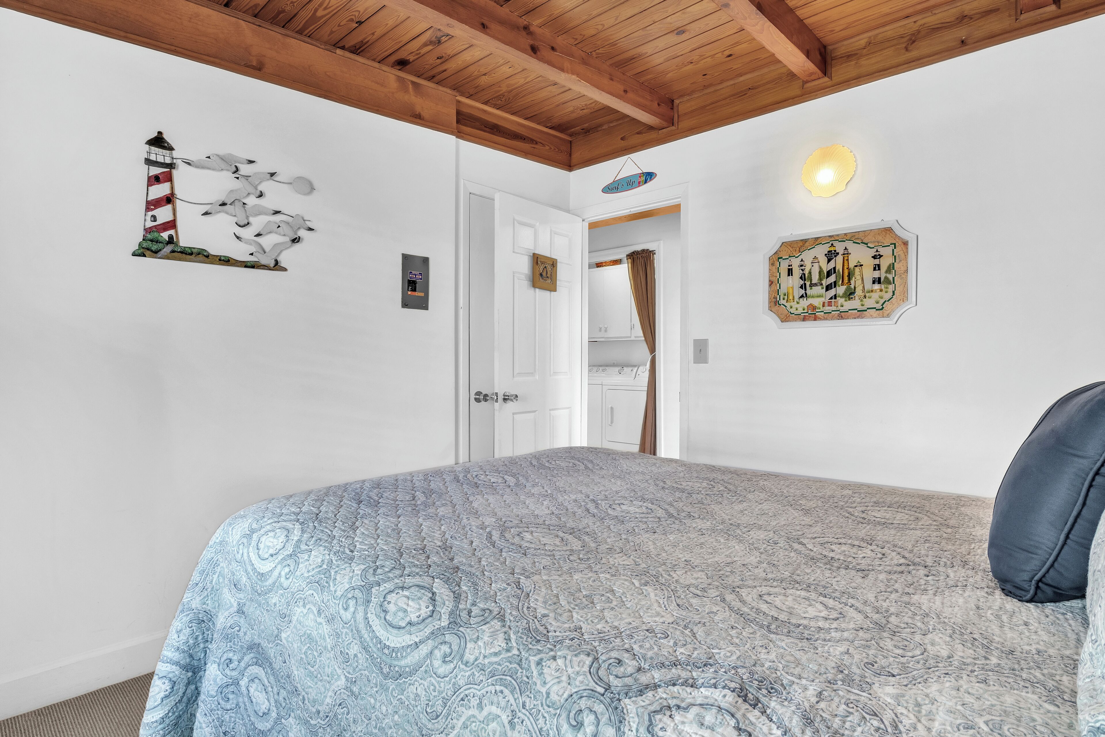 Une chambre à coucher avec un lit, un plafond en bois, une porte blanche et des éléments de décoration murale, notamment une représentation d’un phare et une carte.