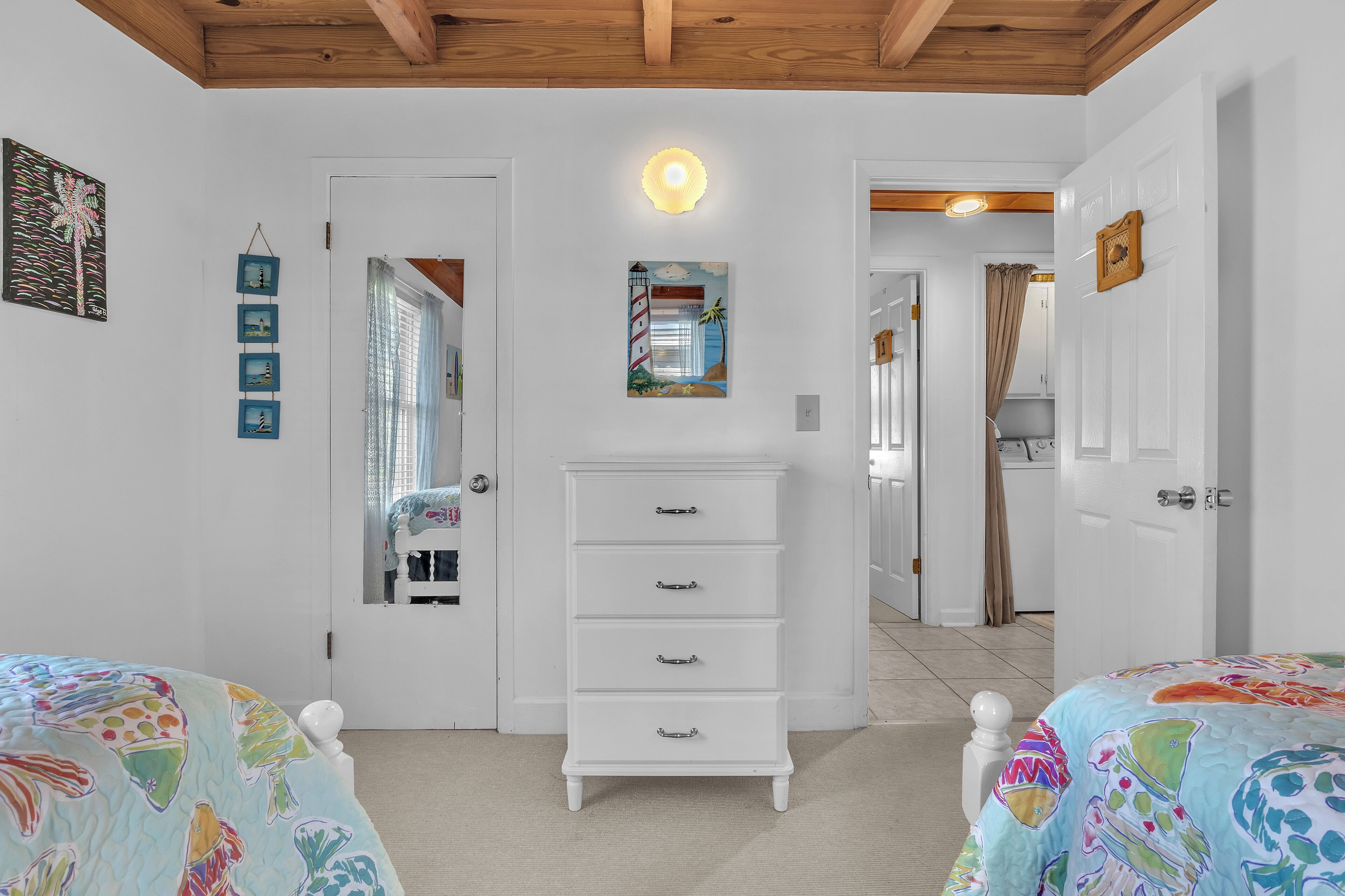 Un dormitorio con un tocador blanco, una cama con colcha de colores, una lámpara de techo y una puerta que da a otra habitación.