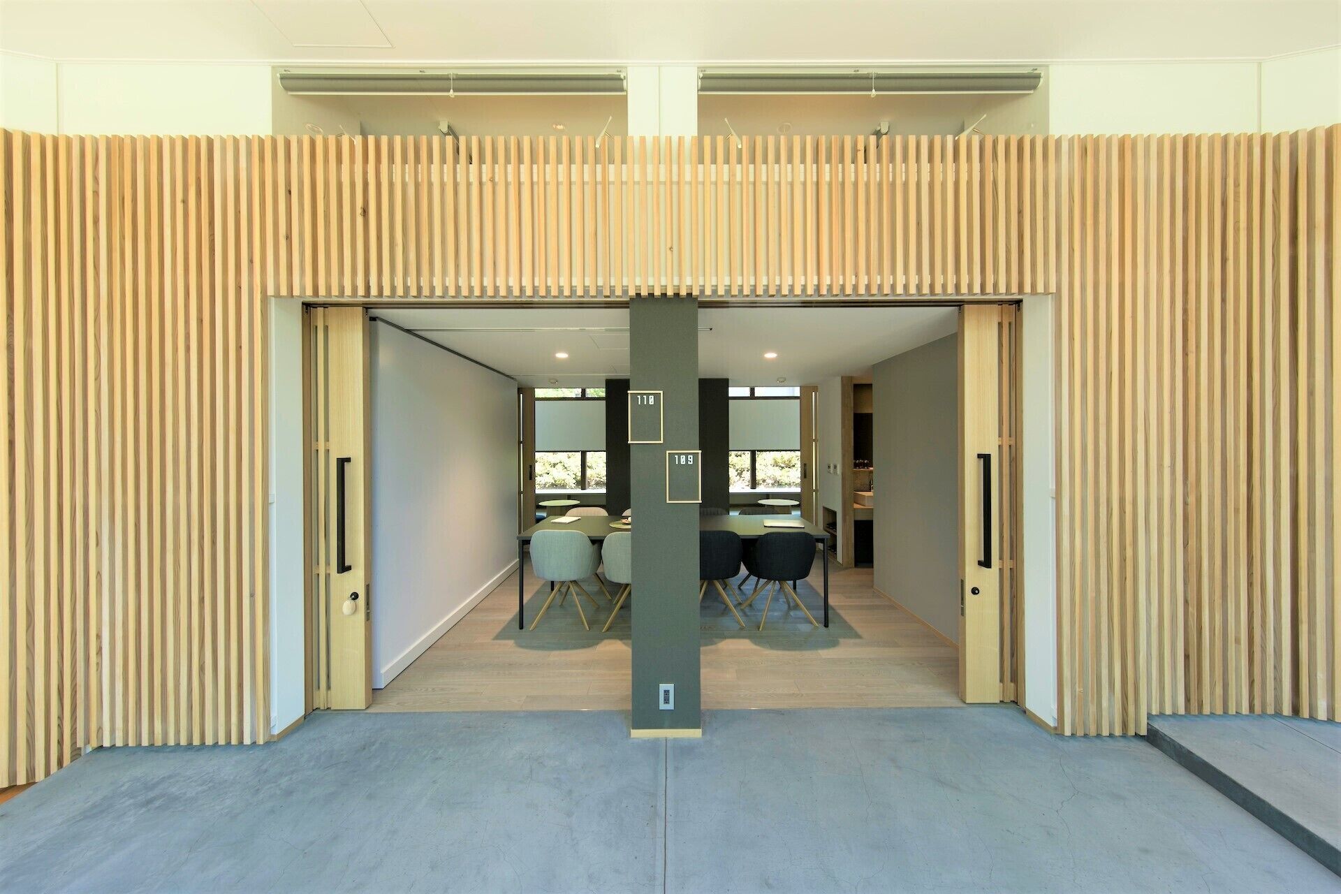 Un intérieur moderne avec un mur à lattes de bois, un pilier central et un espace salon comprenant des tables et des chaises.