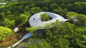 Un bâtiment moderne doté d’un toit incurvé, entouré d’une forêt dense.