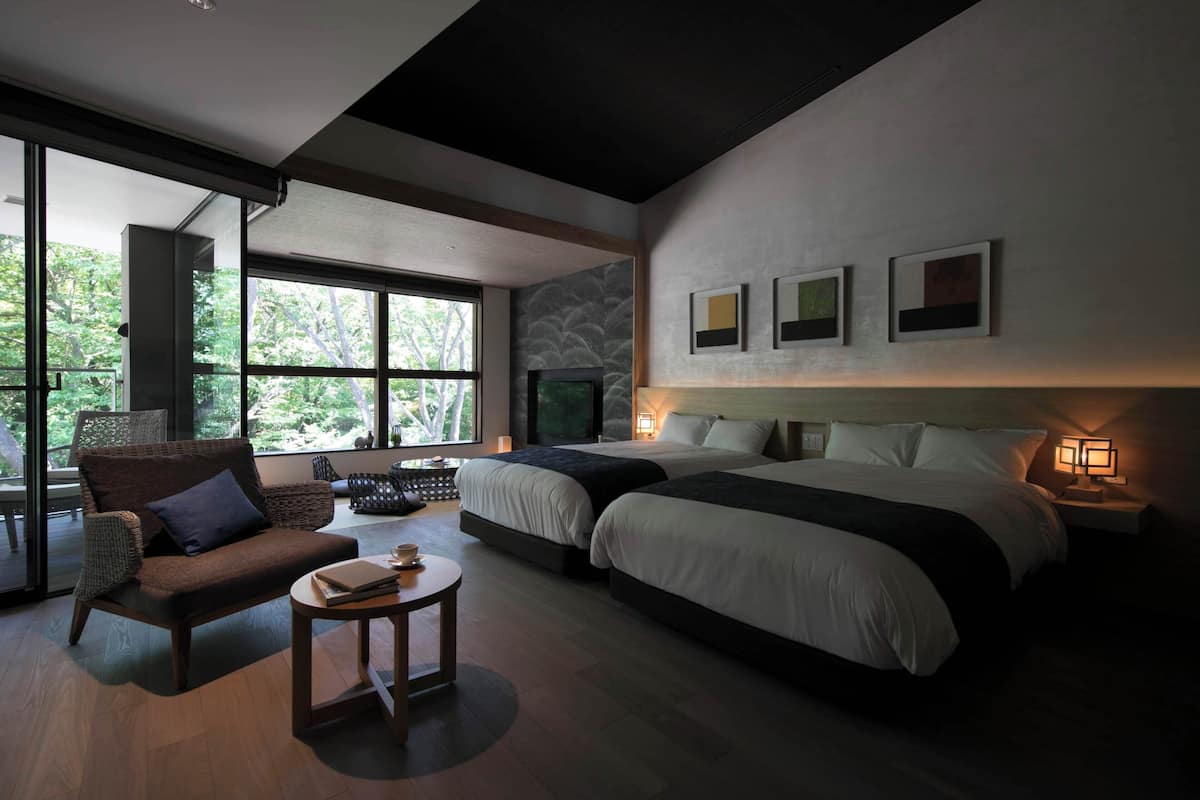 Une chambre d’hôtel moderne avec deux lits, un canapé, une petite table et de grandes fenêtres.